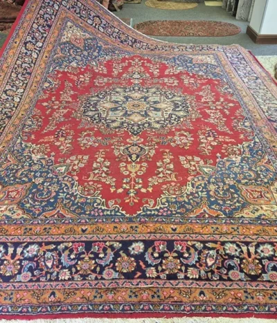 Pre-loved Hand-Knotted Mashad rug, Size: 394 x 304 cm, Central Medallion with a classic Shah Abbasi floral field and elegant corner spandrels (Lachak Toranj), Rich Cochineal Red field contrasted with deep Midnight Blue borders.