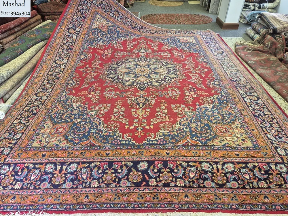 Pre-loved Hand-Knotted Mashad rug, Size: 394 x 304 cm, Central Medallion with a classic Shah Abbasi floral field and elegant corner spandrels (Lachak Toranj), Rich Cochineal Red field contrasted with deep Midnight Blue borders.