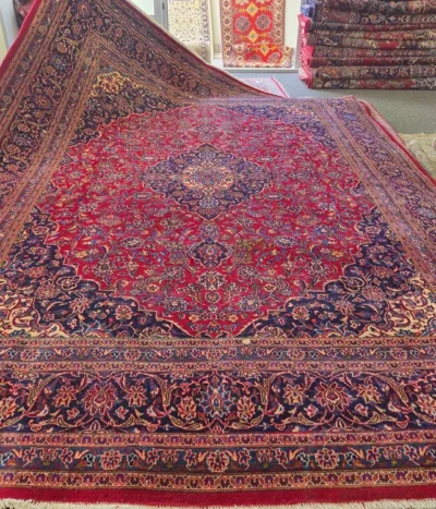 Authentic hand-knotted Kashan rug. size: 395 x 298 cm. Features a striking navy and cream central sunburst medallion set against a rich crimson field, Framed by a wide, detailed navy border with repeating "Shah Abbasi" floral motifs and delicate ivory vine scrolls.