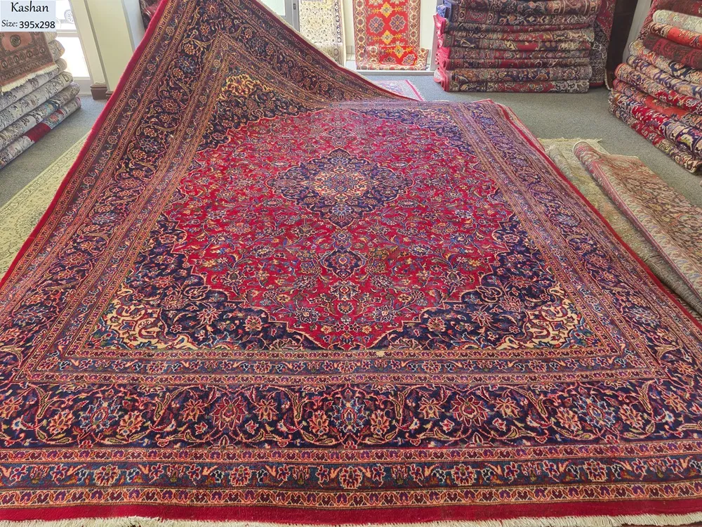 Authentic hand-knotted Kashan rug. size: 395 x 298 cm. Features a striking navy and cream central sunburst medallion set against a rich crimson field, Framed by a wide, detailed navy border with repeating "Shah Abbasi" floral motifs and delicate ivory vine scrolls.