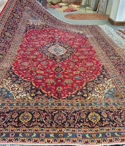 Hand-Knotted Kashan Persian Rug, Size: 384 x 252 cm, Classic Medallion-and-Corner layout featuring a rich, ruby-red field adorned with detailed floral motifs and a deep navy blue border. High-quality, soft wool pile on a sturdy cotton foundation.
