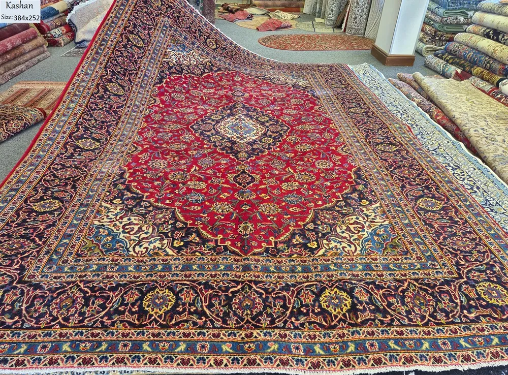 Hand-Knotted Kashan Persian Rug, Size: 384 x 252 cm, Classic Medallion-and-Corner layout featuring a rich, ruby-red field adorned with detailed floral motifs and a deep navy blue border. High-quality, soft wool pile on a sturdy cotton foundation.