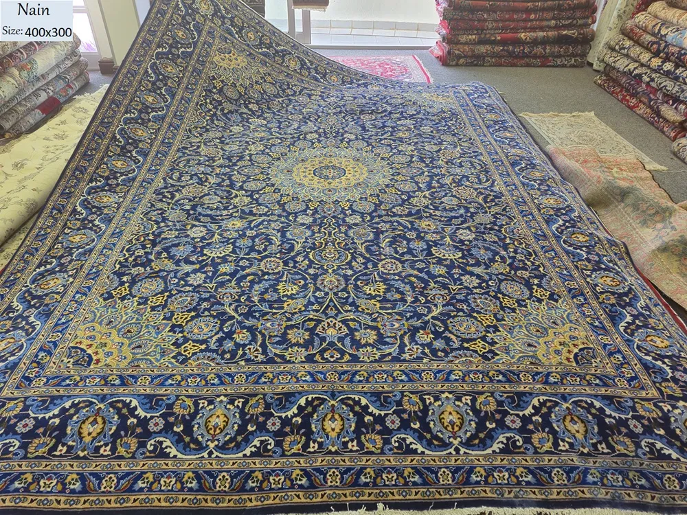 Exquisite  hand-knotted Nain Persian carpet, Size: 400 x 300 cm, features the timeless Shah Abbasi floral motif, Its design is centered around a radiant multi-lobed medallion, adorned with royal blue and gold accents. Crafted from fine Kork wool.