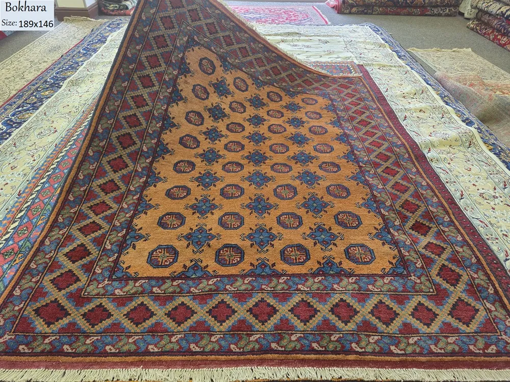 Hand-knotted Bokhara rug, Size 189 x 146 cm, repeating octagonal medallions (Guls) and star motifs, AmberGolden-Orange field with Cobalt Blue, High-quality wool on a durable cotton foundation.