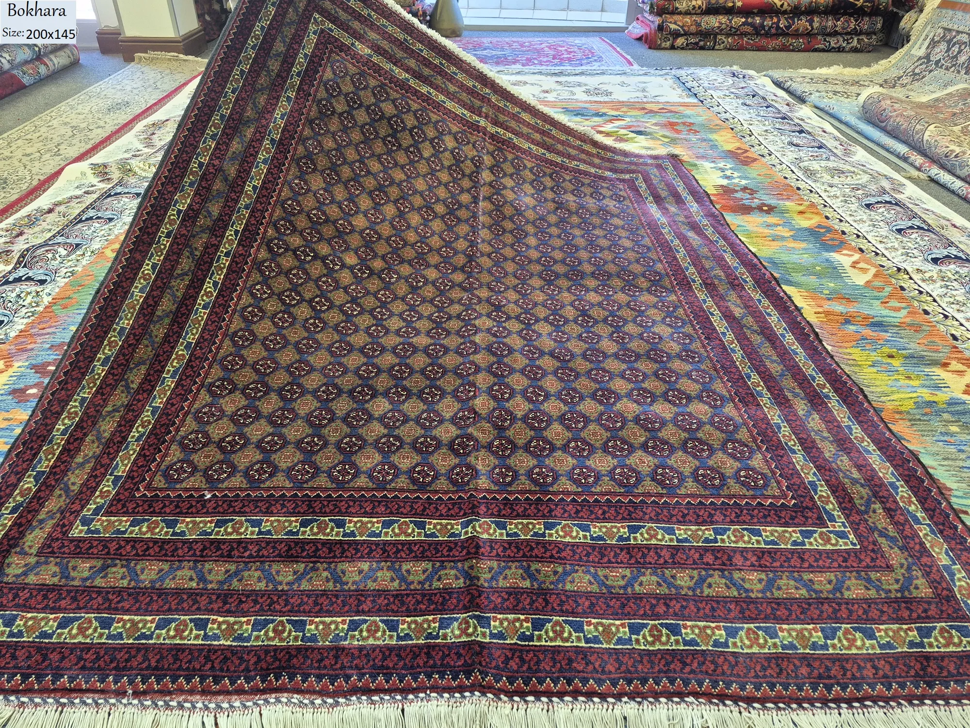 Premium Bokhara rug, Size: 200 x 145 cm, Fine hand-knotted by kurk wool & vegetable dye, Repeating Tekke Gul in a deep burgundy & navy blue foundation is highlighted by vibrant gold & green accents within the geometric borders pattern.