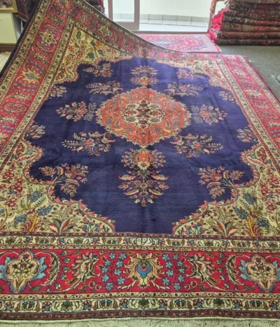 Hand-Knotted Qum Persian Carpet, Size: 390 x 296 cm, an exquisite deep navy-blue field framed by rich crimson & ivory borders. The intricate central medallion is surrounded by delicate floral motifs, scrolling vines, & finely detailed botanical patterns, Artist’s signature woven in, fine knotted by Kurk wool.