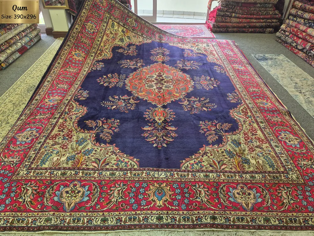 Hand-Knotted Qum Persian Carpet, Size: 390 x 296 cm, an exquisite deep navy-blue field framed by rich crimson & ivory borders. The intricate central medallion is surrounded by delicate floral motifs, scrolling vines, & finely detailed botanical patterns, Artist’s signature woven in, fine knotted by Kurk wool.