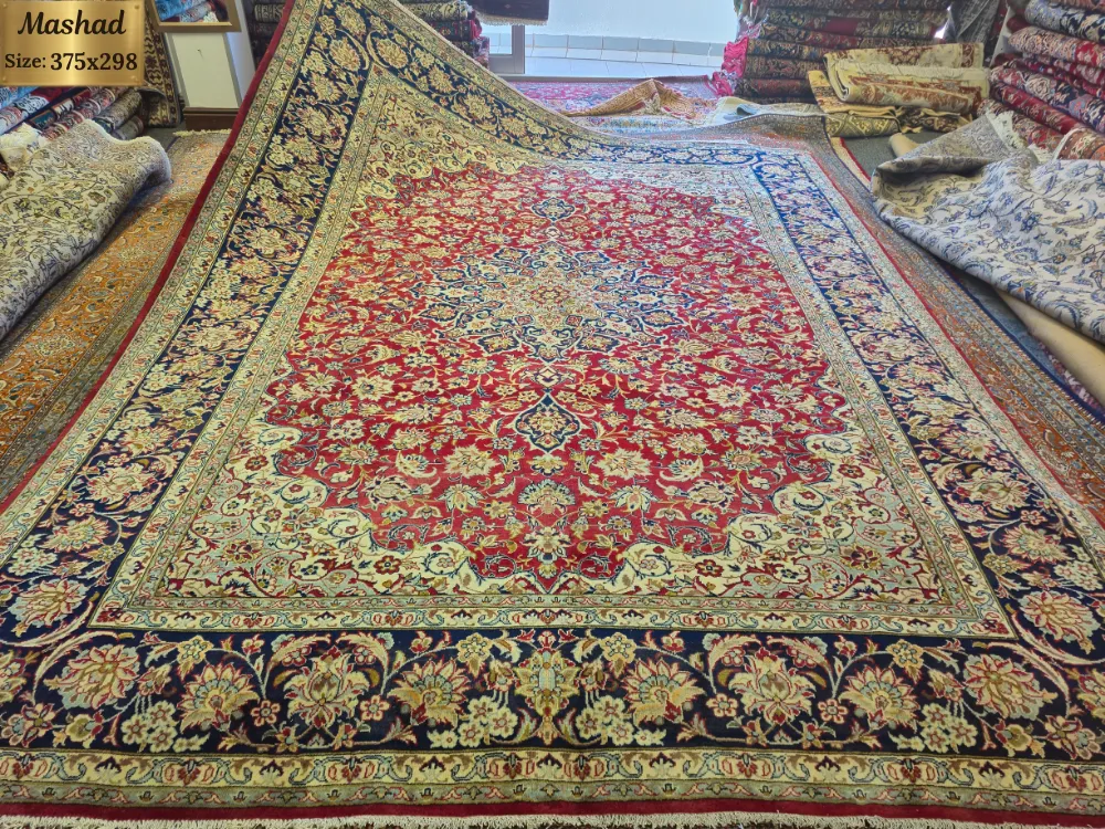 Hand-knotted Mashhad Persian Carpet, Size: 375 x 298 cm, rich red field adorned with intricate floral and scrollwork motifs, beautifully contrasted by a deep navy blue and ivory border, wool on a cotton foundation.